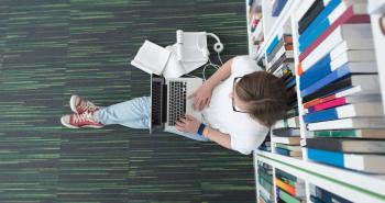 Student sitting with laptop and leaning against bookcase