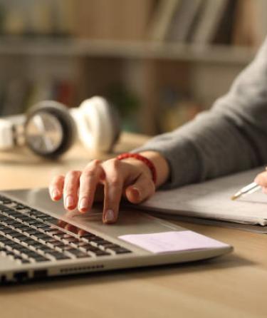 Hands holding pen and typing on laptop