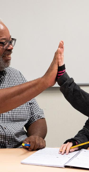 College staff member high-fives a smiling student, celebrating an achievement on campus.