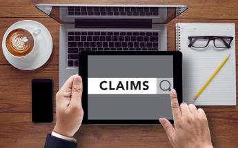 Person searching on tablet for claims over a laptop