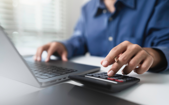 Person using a calculator and laptop at a desk.