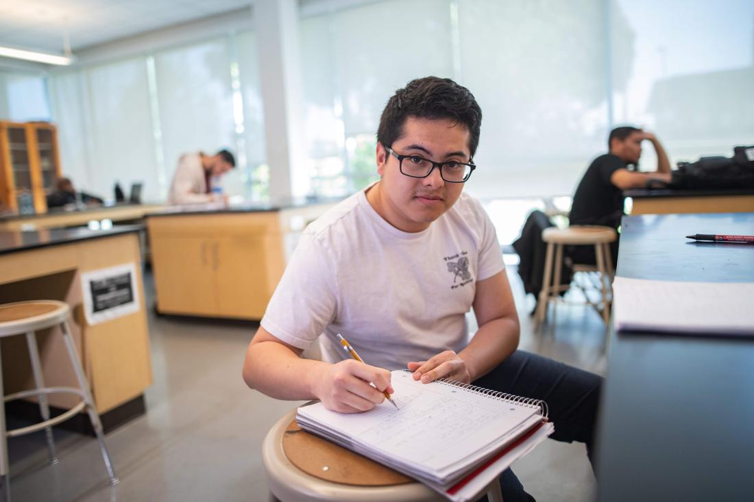 Student sitting in a classroom writing on a notebook