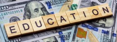 Photo of Scrabble tiles spelling 'Education' placed on top of U.S. dollar bills.