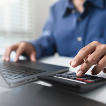 Person using a calculator and laptop at a desk.